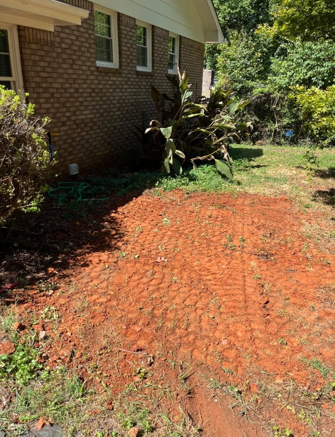 Backyard red clay graded and leveled after excavation beside a brick house