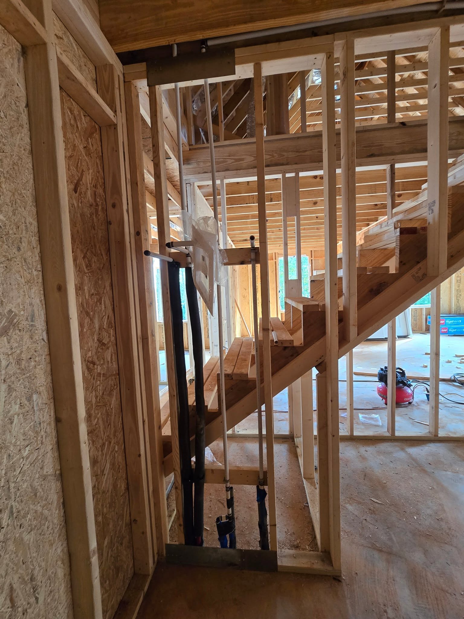 PEX and insulated supply lines run through wall framing beside a staircase