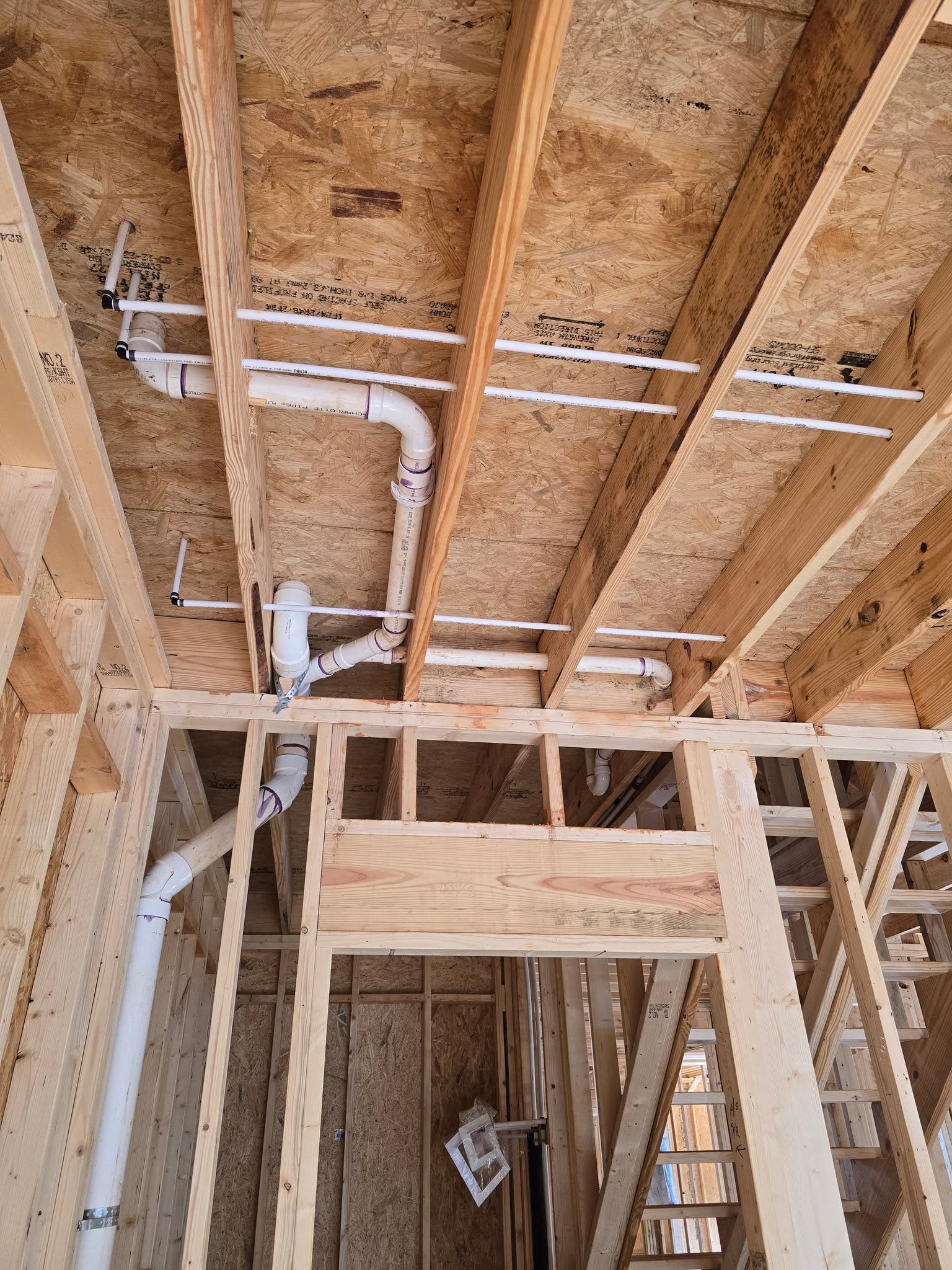 PVC drain and vent piping routed through floor joists on a new build