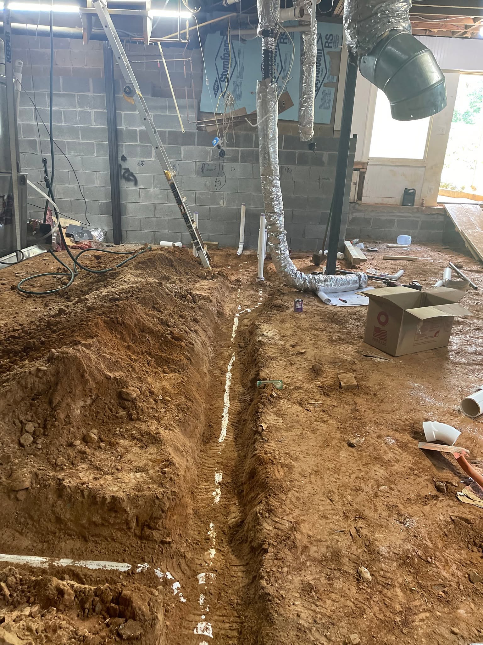 Crawlspace trench with PVC drain laid in red clay under the home