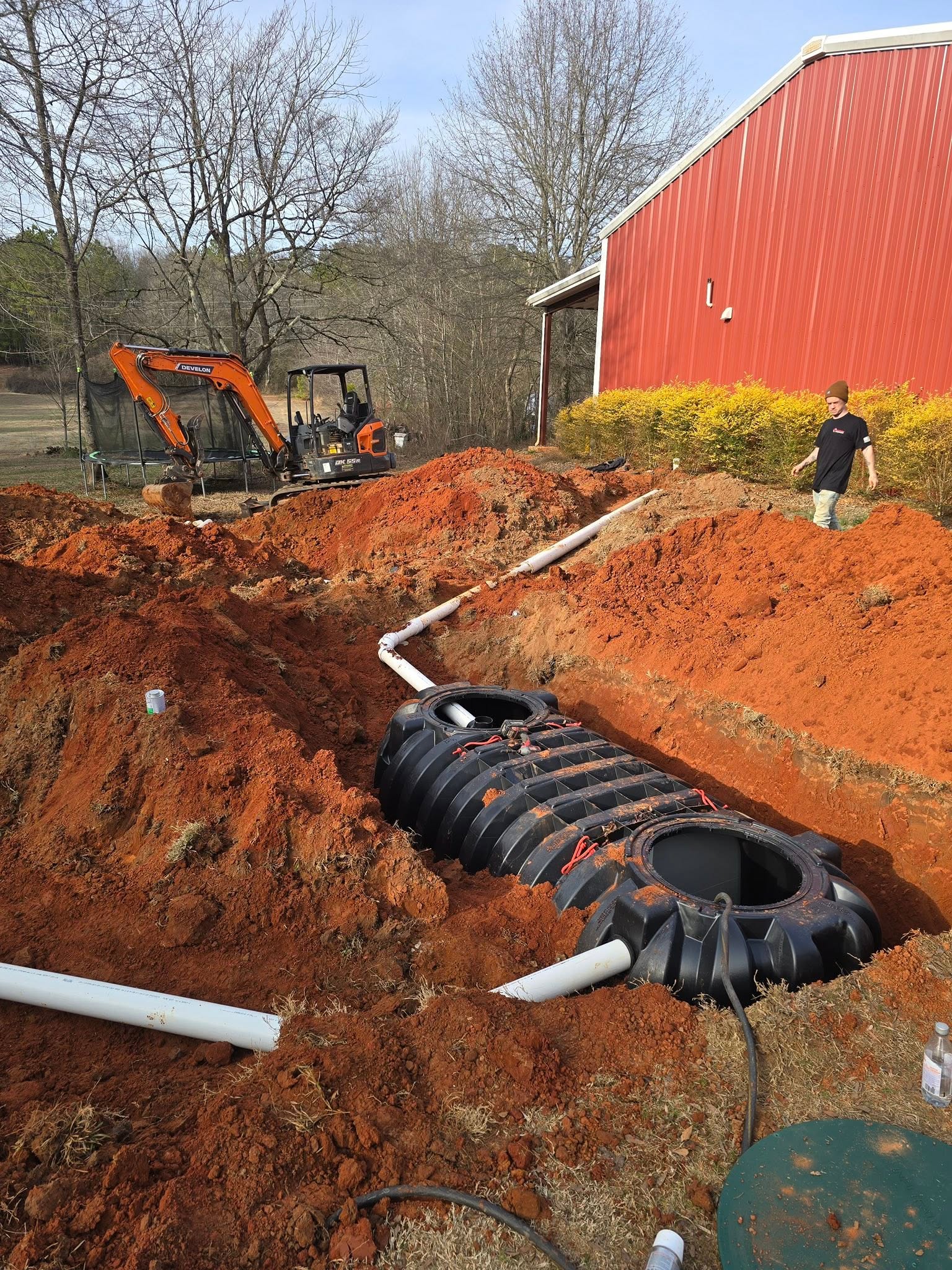 New black septic tank set in red clay with PVC lines connected — North Georgia