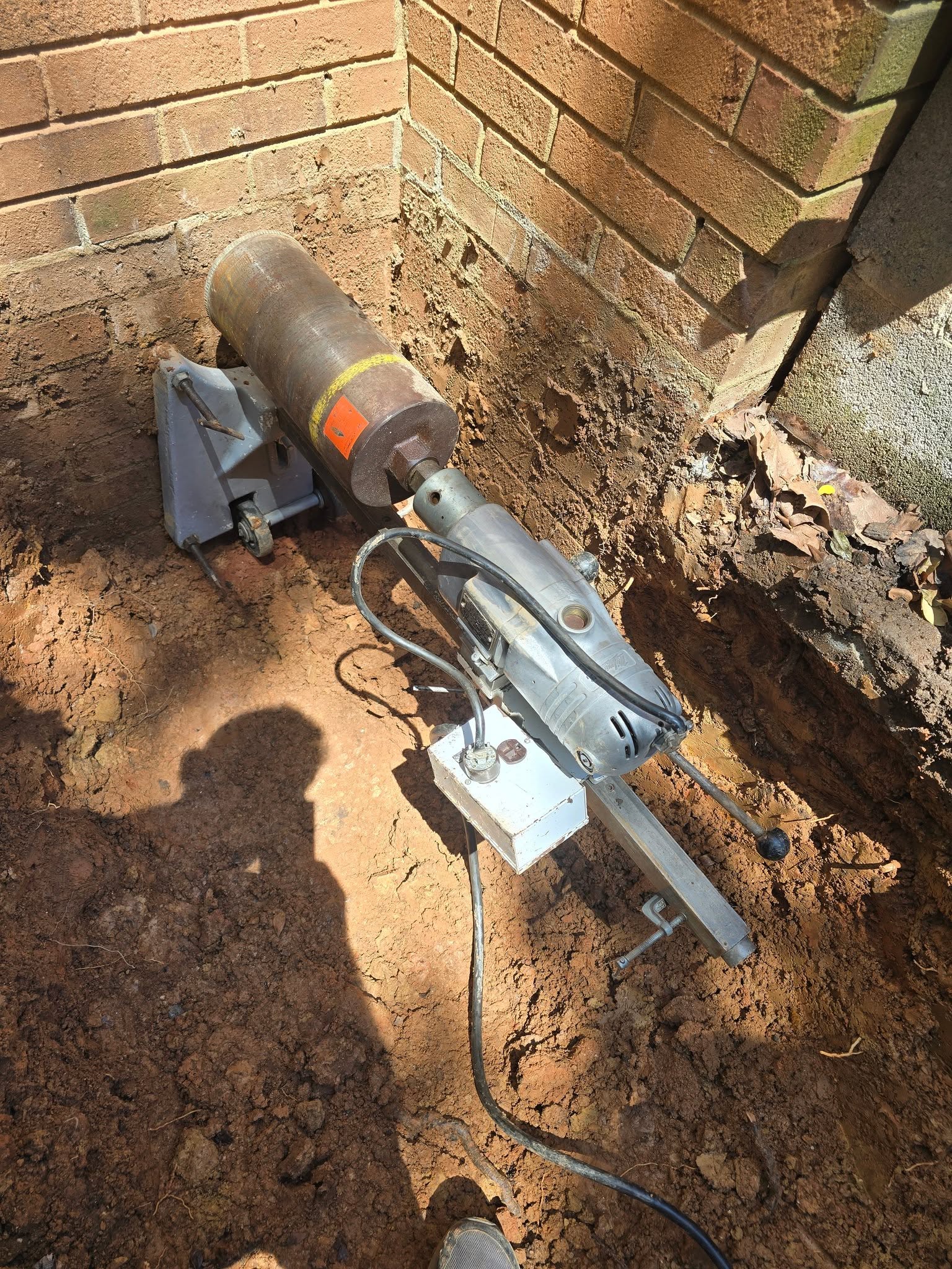 Core drill set in a trench to bore a utility opening through a brick foundation